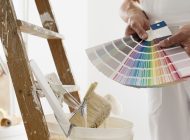 hands of house painter man decorator choose the color using the sample swatch, work of the house to renovate, a wooden ladder with paint brushes and a bucket as a background, close up